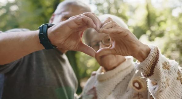 Hände einer Pflegeperson und einer älteren Frau formen gemeinsam ein Herz